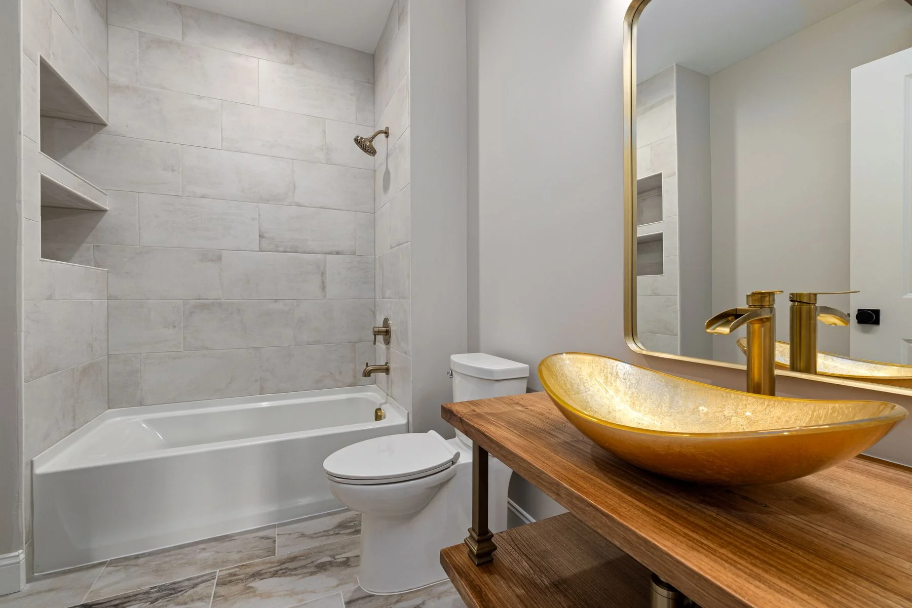 Bathroom with marble-look tile, warm wood vanity and gold fixtures
